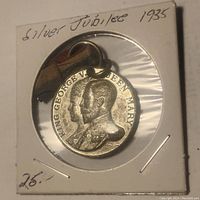 Front image of 1935 Silver Jubilee medal showing embossed profiles of King George V and Queen Mary with original ribbon attached, inside 2x2 holder.