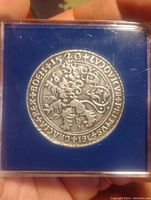 Back side of the pewter coin with crowned figure and inscriptions in a plastic holder labeled 'the WORLD'S first COIN'.