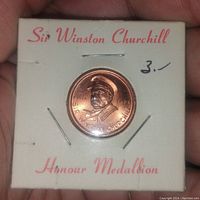 Front side of the Sir Winston Churchill Honour Medallion showing raised profile and dates 1874-1965, mounted on a white card with red text.