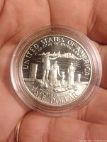Reverse side of the coin depicting an immigrant family arriving by ship with the New York skyline in background, with inscriptions UNITED STATES OF AMERICA, A NATION OF IMMIGRANTS, E PLURIBUS UNUM, HALF DOLLAR.