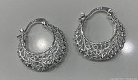 Close-up of the silver plated hoop earrings lying on a flat surface, showing intricate openwork design and hinged clasp closure
