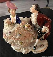 Front angled view showing the woman in pink lace skirt and the man in maroon coat, seated on detailed base.