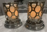 Pair of silver metal hurricane candle holders viewed from front, showing hexagonal geometric pattern enclosures with candles inside (candles not included).