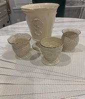 Lenox ceramic vase and three candle holders with gold trim displayed atop six white Maxwell Williams placemats with gold threading on a table