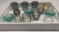 13 glass tealight candleholders in various colors and patterns on a white serving tray