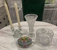 All four items together on a white marble table: crystal double candleholder with two candles, crystal vase, crystal candy dish, and German floral trinket box.