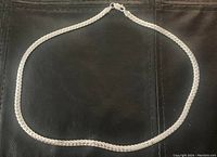 Full view of the 20 inch silver chain necklace lying flat on black surface.