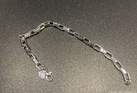 Silver plated link bracelet laid out on black surface showing the rectangular chain links and round charm near lobster clasp.