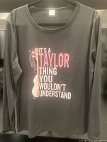 Front view of gray long sleeve Taylor Swift T-shirt showing graphic text and design.