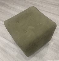 Green microfiber square ottoman footstool viewed from an angle showing the button tufting detail on top and smooth rounded edges.