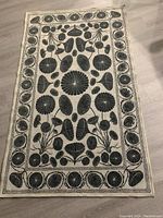 Full view of the cream and black botanical patterned rug laid out on flooring.