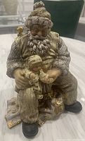 Angle showing Santa holding baby on lap seated in striped pants and gold vest with gifts around feet
