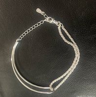 Full view of the sterling silver double knot bracelet with chain and clasp visible on black leather background