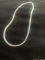 Full view of silver necklace laid flat on black surface.