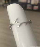 Photo showing silver ring fashioned in a branch style with small branch details, placed on a white ring holder against a blurred background.