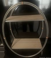 Front perspective of the two-tier floating shelf unit showing silver metal circular frame and two whitewashed wood shelves