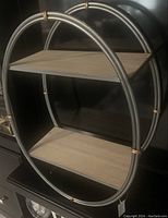 Front angled view showing two-tier shelving unit with circular silver metal frame and whitewashed wood shelves.