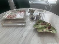 Photo showing full lot from above with all items on a marble table: Fitz and Floyd floral tray, floral piggy bank, Avon butterfly dish, Amour floral tray, E. German pedestal dish, and teapot salt and pepper shakers.
