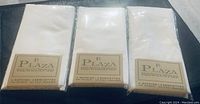 Three unopened packages of Plaza brand white dinner napkins, each package contains four napkins.