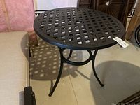 Full view of the black metal round pedestal table with lattice pattern top, showing three curved legs and base support ring.