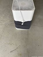 Front view of air purifier showing top perforated grill and lower gray section