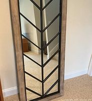 Front view of the tall decorative mirror with wooden frame and black metal wishbone pattern