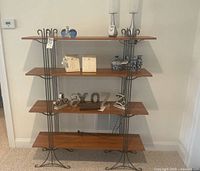 Front view of modern style four-tier shelving unit with wood shelves and black metal frame, some decorative items placed on shelves but not included in sale.