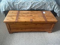 Front view of large wooden chest showing wood grain and leather straps with brass studs.