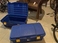 One Rubbermaid tote open, showing interior, with another closed tote nearby on floor in basement setting.