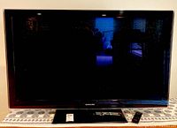 Front view of the Samsung flat-screen TV showing the screen, bezel, stand, and remote control.