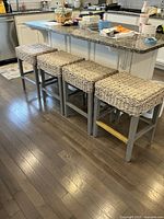 Four grey wooden frame stools with woven seats under kitchen island