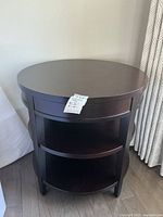 Full front view of the round table showing pullout drawer closed and three curved lower shelves for storage.