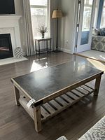 Coffee table displayed in living room with black stone top and rustic solid wood frame with bottom shelf.