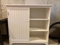 Front view of white cabinet showing one side open shelves and left side door closed with beadboard paneling