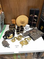 Overall view of the Asian themed lot comprising ceramic tea set, brass dragon figures, wooden carved panel, wooden bowls, metal elephant pot, and opium scale.