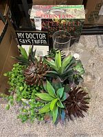 Photo showing multiple artificial succulent plants, a decorative sign, and the boxed Water Bell Fountain on carpeted floor.