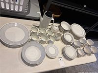 Full view of both dish sets, showing plates, bowls, cups, serving pieces including coffee pot, cream and sugar set in two distinct styles.