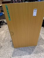 Side view of rectangular folding table standing upright showing wood-grain finish with printed measurement and protractor markings along the side edge.