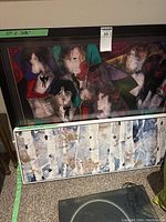 Colorful framed abstract art print depicting stylized group of people in bright colors, measured 37 by 20 inches as shown on the green tape on the frame.