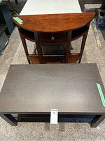 Half moon console table in warm wood finish and rectangular dark wood coffee table next to each other on carpeted floor