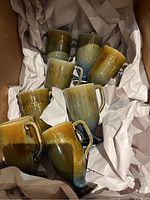 Set of 8 Irish coffee mugs with varying green, blue, and brown glazes, handled with gold embossed 'Irish Coffee' text.