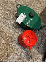 Both green Le Creuset oval Dutch oven and red enamel saucepan with wooden handle