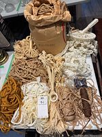 Full lot image showing assorted macrame ropes and hangers with a bag labeled 'MACRAME' containing cords, displayed on a table.
