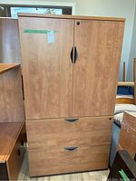 Front view of office cabinet showing two closed doors on top and two closed drawers below, all wood finish with black handles.