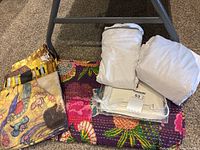 Four pillow covers, hand quilted blanket, and wrapped fitted king sized sheet and king pillowcases all laid out on floor.