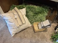 Two green yak hair pillows, white pillow form, beige woven throw scarf with fringes, two small baskets, and hanging shoe rack on carpeted floor.