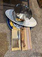 Overall photo showing the large stainless steel pot with lid on top of a large white oval tray, set of six Laguiole steak knives in a wooden box, and two wooden cutting boards