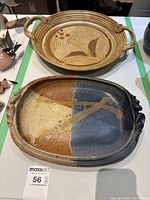 Two pottery trays on a table; one round with leaf motif signed Ernst, one rectangular glazed in brown and blue signed Stewart.