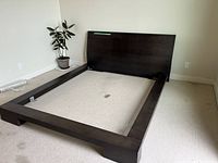 Full view of assembled queen platform bed frame with headboard, placed on carpeted floor next to a potted plant.