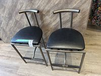 Two matching black metal counter stools with curved backrests and cushioned seats on a wood floor.